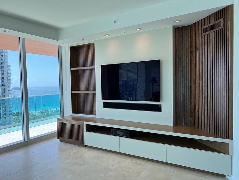 Modern living room with TV and wooden paneling, ocean view through large windows.