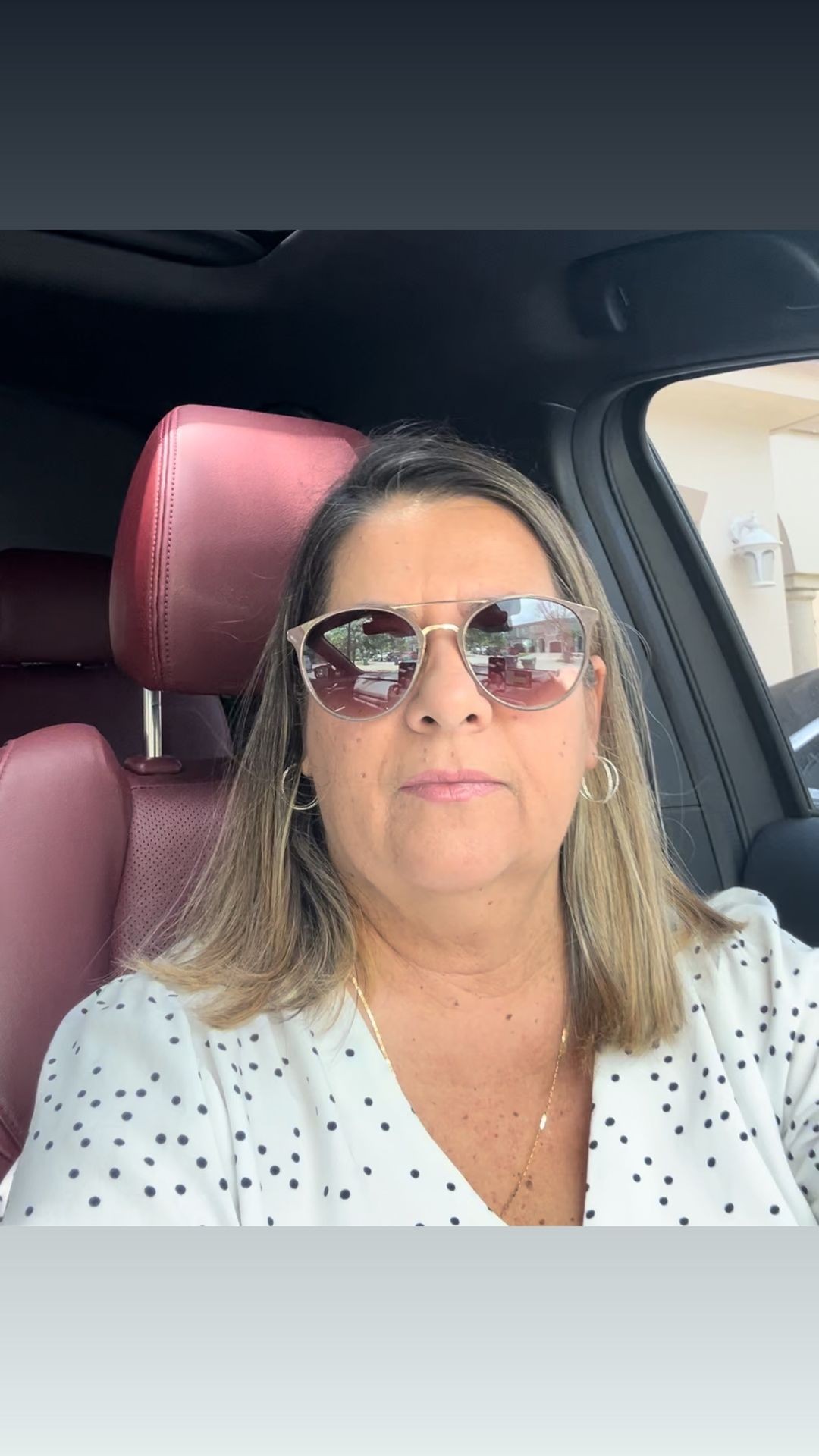 Woman in sunglasses sitting in a car with a red leather seat.