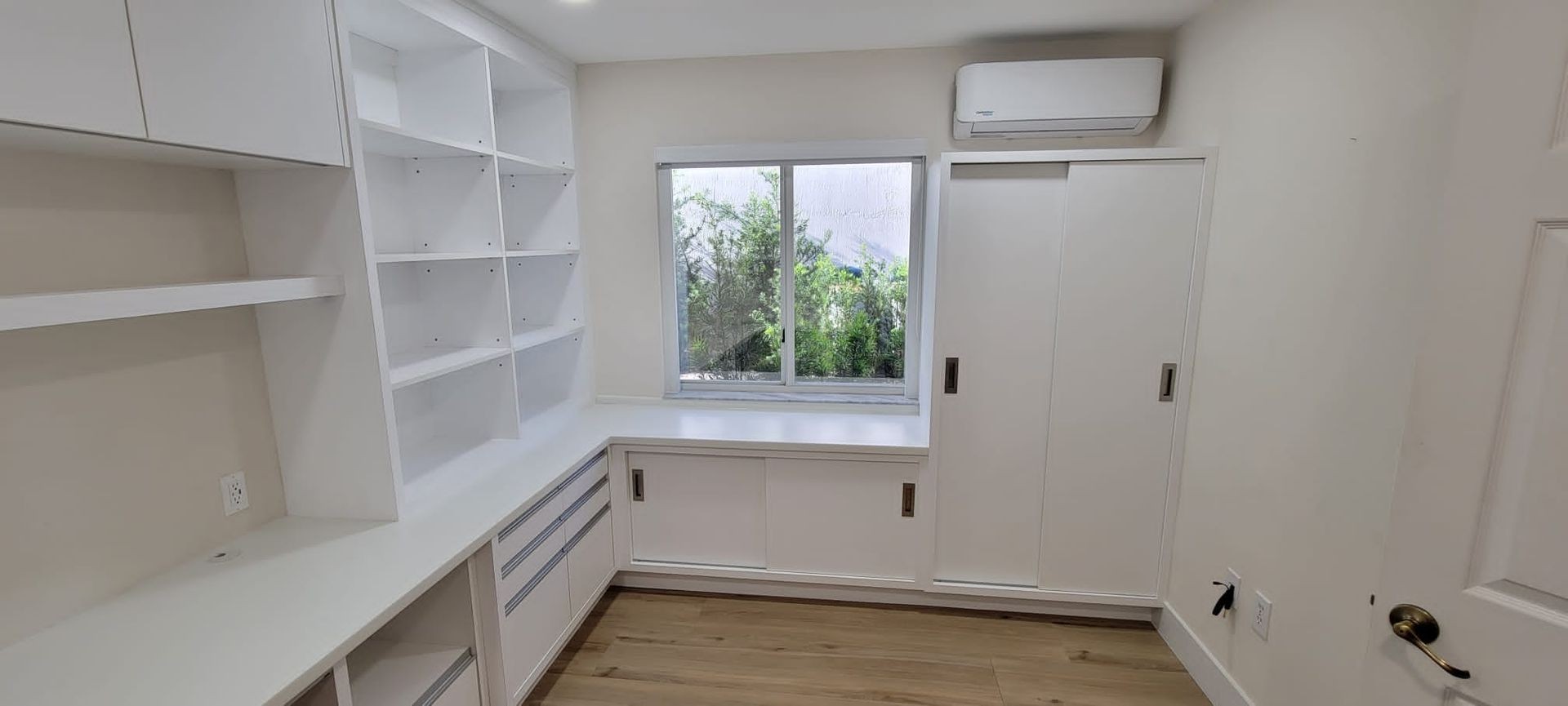 White cabinetry and built-in shelves in a small room with wooden floor and window view.